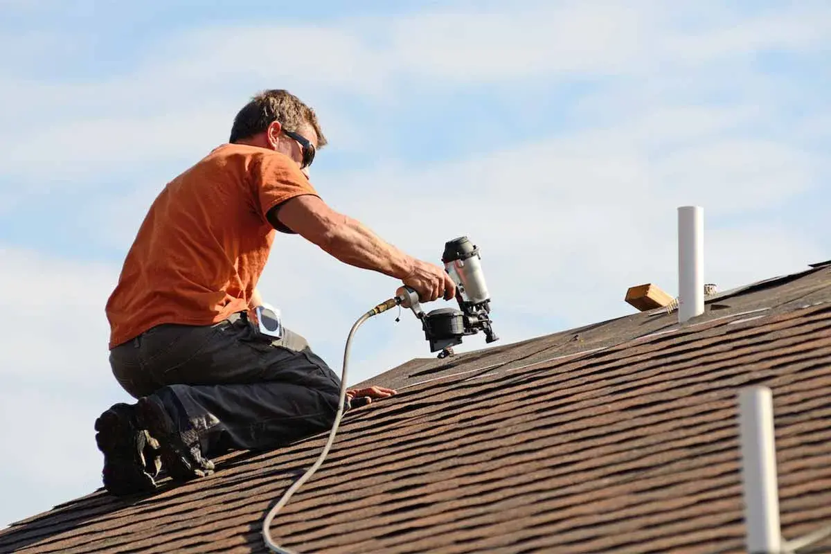 Roofer using a nail gun to install asphalt shingles